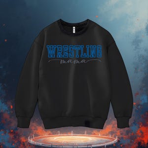 May include: Black sweatshirt featuring the text "WRESTLING mama" in blue and grey script. The sweatshirt is set against a backdrop of a wrestling ring and a fiery, cloudy sky. A crew neck sweatshirt.