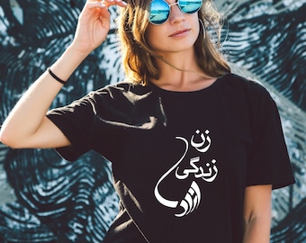 May include: A black t-shirt with white Arabic text that reads "I am a woman who loves life". The model is wearing the shirt and has blue sunglasses on.