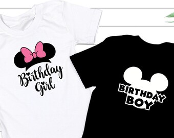 May include: Two short-sleeved t-shirts. One is white with a black Mickey Mouse ear design and a pink bow, with the words "Birthday Girl" in script. The other is black with a white Mickey Mouse ear design and the words "Birthday Boy".
