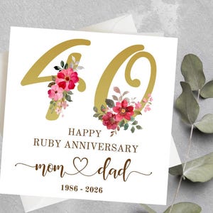 Puede incluir: Tarjeta blanca con el número dorado '40' adornada con arreglos florales. La tarjeta dice 'Happy Ruby Anniversary' y 'mamá y papá' con los años '1986-2026'. La tarjeta está colocada sobre un sobre blanco.