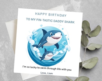 May include: A birthday card with a cartoon shark theme. The card features two blue sharks in a blue water background with the text "HAPPY BIRTHDAY TO MY FIN-TASTIC DADDY SHARK". The card also includes the text "I'm so lucky to swim through life with you. Love, Liam."
