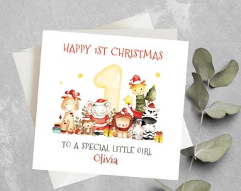 Op de afbeelding: Een witte wenskaart met de tekst "HAPPY 1ST CHRISTMAS" en "TO A SPECIAL LITTLE GIRL. Olivia". De kaart toont aquarel illustraties van feestelijke dieren, waaronder een giraf, een olifant en een zebra, allemaal met kerstmutsen.