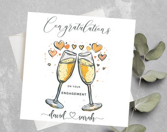 May include: A white card with the text "Congratulations on your engagement" and a drawing of two champagne glasses clinking with hearts and confetti. The names "david & sarah" are written at the bottom of the card.