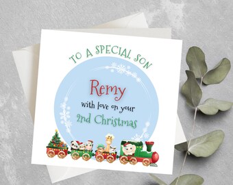 May include: A blue and white Christmas card with a train carrying animals and a Christmas tree. The card says "To a special son Remy with love on your 2nd Christmas".