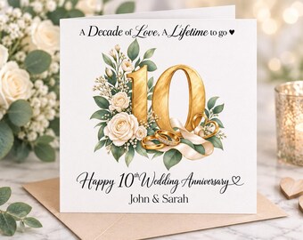 May include: A square white greeting card featuring the text A Decade of Love, A Lifetime to go and Happy 10th Wedding Anniversary with the names John & Sarah. The design includes a large gold number 10, cream roses, green leaves, and gold rings.
