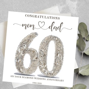 Può includere: Un biglietto bianco con le parole "Congratulazioni Mamma e Papà" e un grande "60" fatto di abbellimenti argentati. Il biglietto celebra un anniversario di matrimonio di diamante, con gli anni 1966-2026 stampati in basso. Il biglietto è su una superficie grigia.