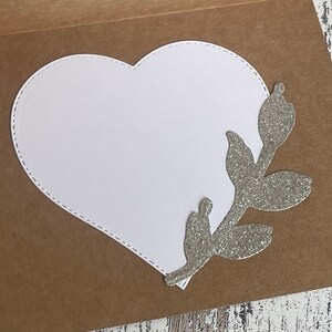 May include: A brown card with a white heart-shaped cutout and a silver glitter branch with leaves on the right side.