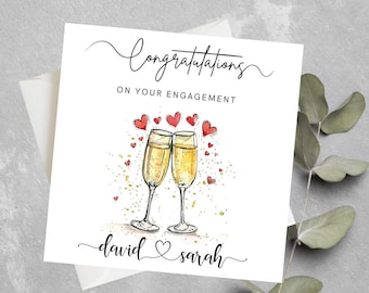 May include: A white card with the text "Congratulations on your engagement" and a drawing of two champagne flutes with red hearts and gold glitter. The names "david & sarah" are written at the bottom of the card.
