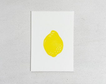 Könnte beinhalten: Gelbe Zitronenillustration auf einer weißen Karte. Die Zitrone hat eine einfarbige Farbe mit kleinen weißen Punkten, vor einem neutralen Hintergrund. Das Kunstwerk ist einfach und grafisch, geeignet für Küchen- oder Food-Dekorationen.