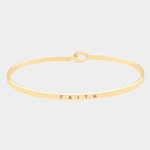 May include: A gold bangle bracelet with a heart-shaped clasp and the word "FAITH" engraved on the band.