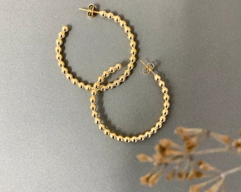 May include: A pair of gold hoop earrings made of small, round beads.