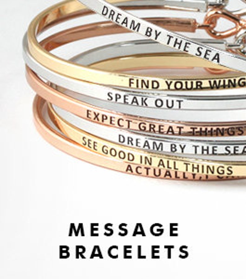 May include: A stack of gold, silver, and rose gold bangle bracelets with inspirational messages engraved on them. The messages include "Dream by the Sea", "Find Your Wing", "Speak Out", "Expect Great Things", "Dream by the Sea", "See Good in All Things", and "Actually". The bracelets are stacked on top of each other and the messages are visible on each bracelet. The bracelets are called "Message Bracelets".