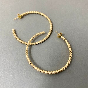 May include: A pair of gold hoop earrings made of small beads. The earrings are about 2 inches in diameter.