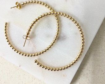 May include: A pair of gold hoop earrings with a beaded design. The earrings are large and have a diameter of approximately 2 inches.