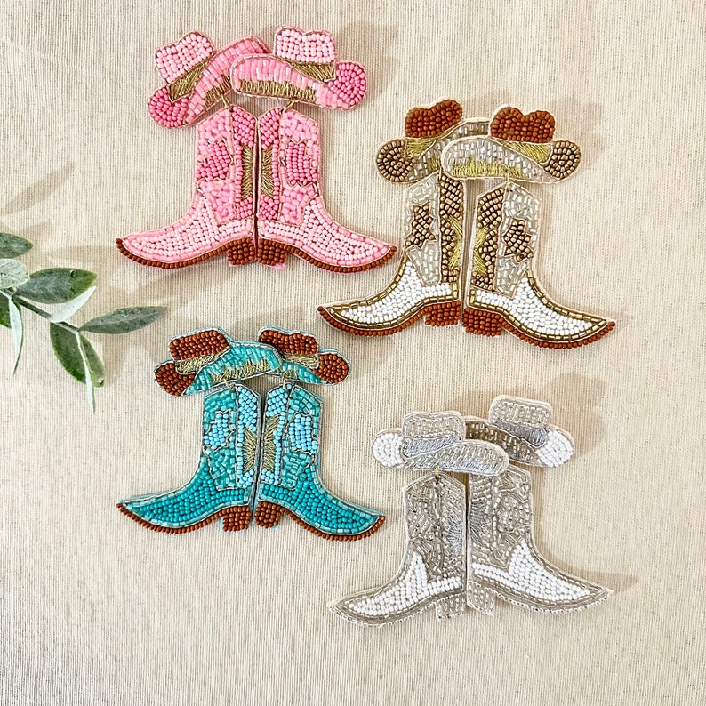 K&ouml;nnte beinhalten: Drei Paar Perlen-Cowboy-Stiefel-Ohrringe. Das erste Paar ist pink, das zweite t&uuml;rkis und das dritte wei&szlig;.