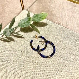 Op de afbeelding: Een paar blauwe en gouden creolen. De oorbellen zijn gemaakt van gemarmerd materiaal en hebben een gouden afwerking.