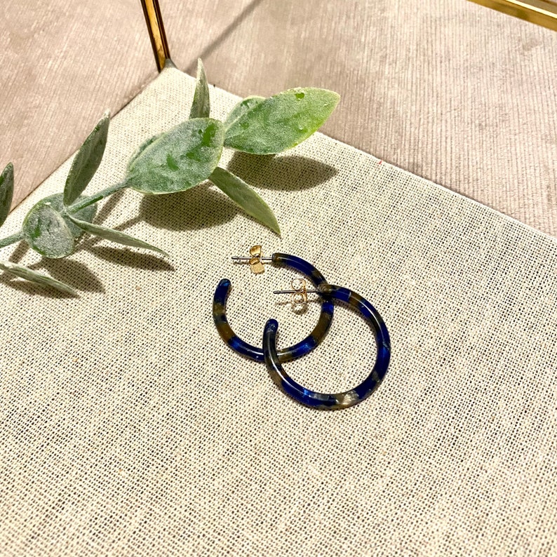 Op de afbeelding: Een paar blauwe en gouden creolen. De oorbellen zijn gemaakt van gemarmerd materiaal en hebben een gouden afwerking.