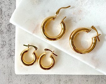 May include: Three pairs of gold hoop earrings of different sizes. The earrings are on a white marble surface.