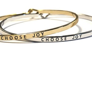 May include: Two gold and silver bangle bracelets with the words "Choose Joy" engraved on them.