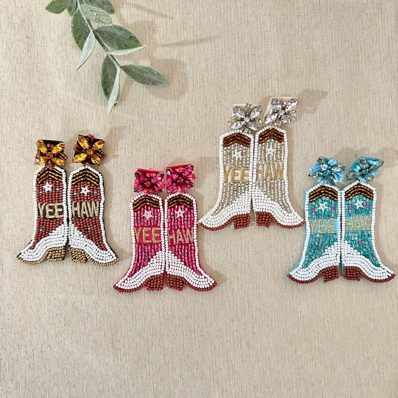 K&ouml;nnte beinhalten: Vier Paar Perlenohrringe in Form von Cowboy-Stiefeln in verschiedenen Farben. Die Ohrringe sind wei&szlig; mit goldenen Akzenten und den Worten "Yee Haw" auf den Stiefeln. Die Farben sind Gold, Pink, Blau und T&uuml;rkis.
