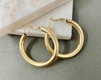 May include: A pair of gold hoop earrings with a smooth, matte finish. The earrings are large and have a simple, classic design.