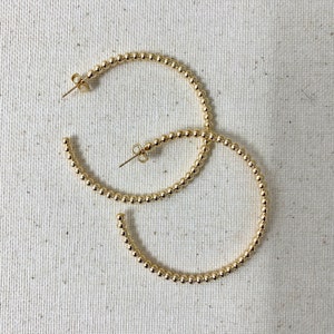 May include: A pair of gold hoop earrings made of small, round beads. The earrings are large and have a simple, elegant design.