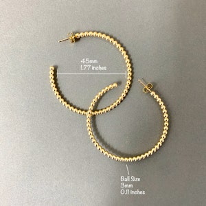 May include: A pair of gold hoop earrings with a beaded design. The hoops are 1.77 inches in diameter and the beads are 0.11 inches in diameter.
