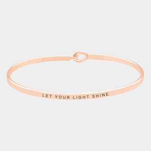 May include: Rose gold bangle bracelet with the inscription "Let your light shine".