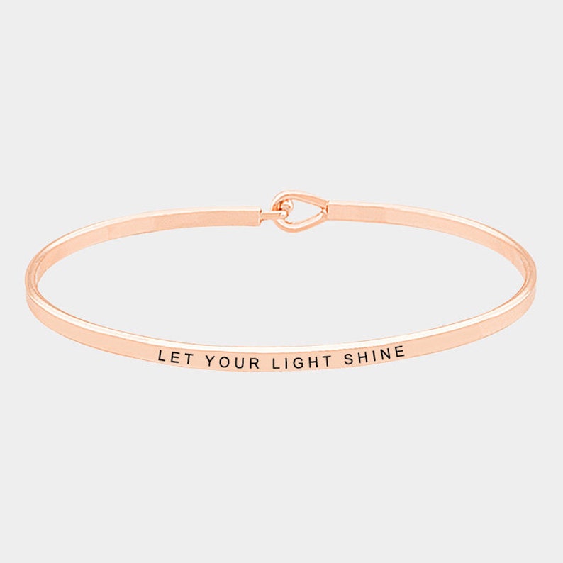 May include: Rose gold bangle bracelet with the inscription "Let your light shine".