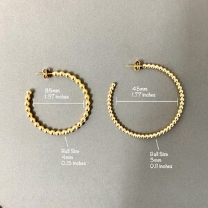 May include: Two gold hoop earrings with a beaded design. The smaller hoop is 1.37 inches in diameter with 4mm beads. The larger hoop is 1.77 inches in diameter with 3mm beads.