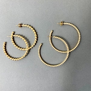 May include: Three pairs of gold hoop earrings with a beaded design. The earrings are all different sizes.