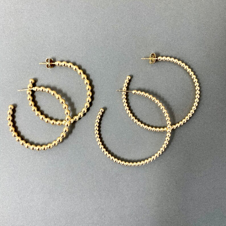May include: Three pairs of gold hoop earrings with a beaded design. The earrings are all different sizes.