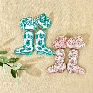 K&ouml;nnte beinhalten: Ein Paar t&uuml;rkisfarbene und wei&szlig;e Perlenohrringe mit Cowboy-Stiefeln und H&uuml;ten sowie ein Paar rosa und wei&szlig;e Perlenohrringe mit Cowboy-Stiefeln und H&uuml;ten.