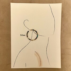 Op de afbeelding: Een paar grote, ronde, veelkleurige oorringen. De oorringen hebben een diameter van 50 mm en hebben een schildpadpatroon met blauwe en groene accenten.