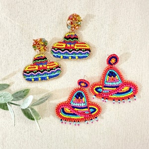 K&ouml;nnte beinhalten: Ein Paar bunte Perlenohrringe in Form von Sombreros. Die Ohrringe sind aus roten, orangefarbenen, gelben, gr&uuml;nen, blauen und violetten Perlen gefertigt. Die Ohrringe sind ein lustiges und festliches Accessoire f&uuml;r jeden Anlass.