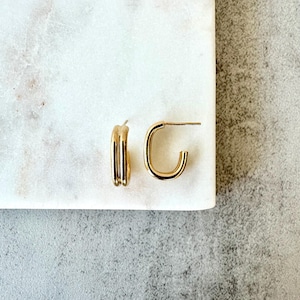 May include: A pair of gold hoop earrings with a simple, modern design. The earrings are made of a thick, rounded wire that is twisted to create a unique look.