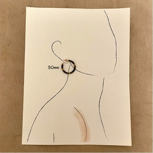 Op de afbeelding: Een paar bruine en zwarte creolen met een diameter van 30 mm. De oorbellen worden getoond op een witte achtergrond met een tekening van een oor.