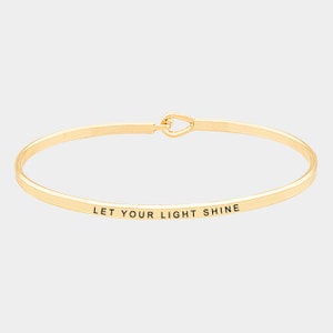 May include: Gold bangle bracelet with the inscription "Let your light shine".