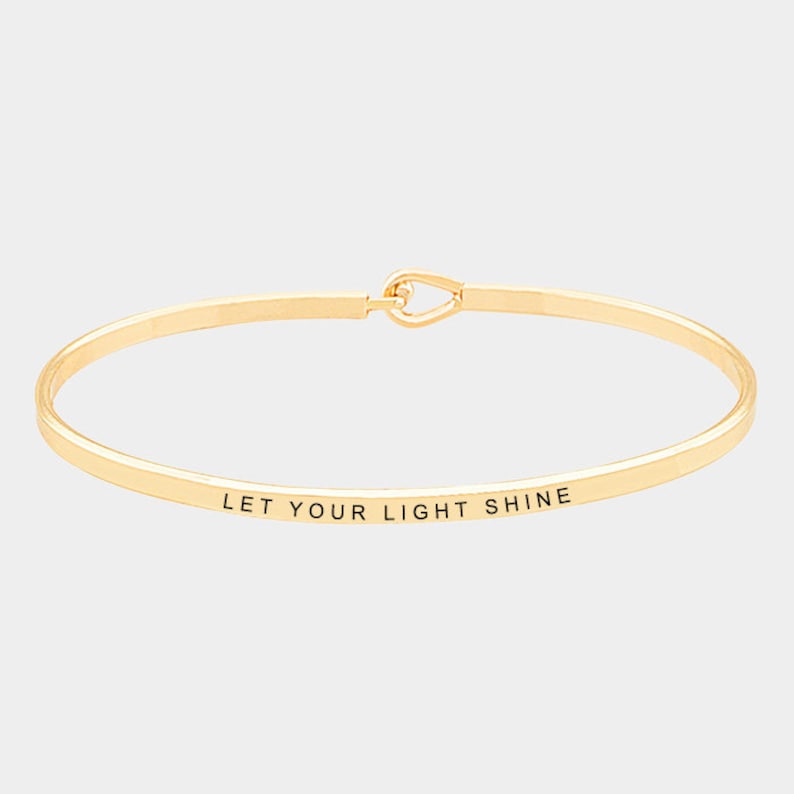 May include: Gold bangle bracelet with the inscription "Let your light shine".