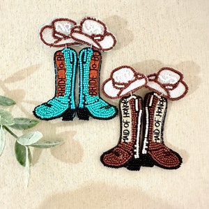 K&ouml;nnte beinhalten: Ein Paar Perlen-Cowboy-Stiefel-Ohrringe mit einem wei&szlig;en Cowboyhut-Anh&auml;nger. Ein Paar sagt "Bride to Be" und das andere sagt "Maid of Honor".