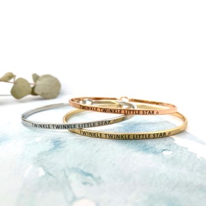 May include: Three silver bangle bracelets with the inscription "Twinkle Twinkle Little Star" on each. The bracelets are stacked on top of each other.