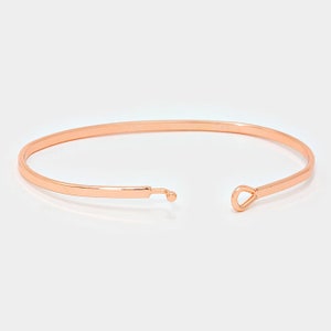 May include: A rose gold bangle bracelet with a simple, minimalist design. The bracelet has a small, round clasp on one end and a teardrop-shaped opening on the other.
