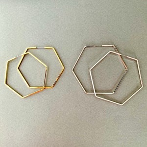 May include: Two pairs of hexagonal hoop earrings, one pair is gold and the other is silver.