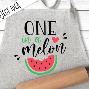 May include: A gray apron with the text "ONE in a melon" and a red watermelon slice with green rind and black seeds.