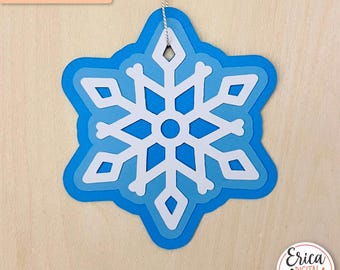 May include: A layered blue and white snowflake ornament with a string for hanging. The snowflake is a digital cut file for paper and cardstock.