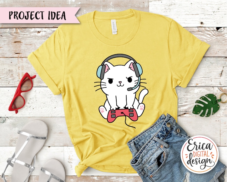 Op de afbeelding: Een geel T-shirt met een cartoon witte kat die een koptelefoon draagt en een videogamecontroller vasthoudt. De tekst "Project Idea" staat op een roze banner bovenaan de afbeelding.