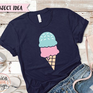 May include: Navy blue t-shirt featuring a colorful ice cream cone design. The ice cream has two scoops, one pink and one blue, with sprinkles on top. The cone is a light brown color. Text on the shirt reads "PROJECT IDEA".