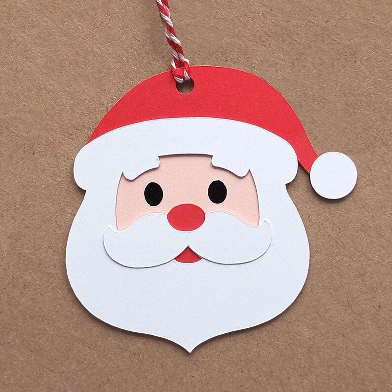Op de afbeelding: Wit papieren kerstversiering in de vorm van het gezicht van de kerstman met een rode muts en een witte baard.