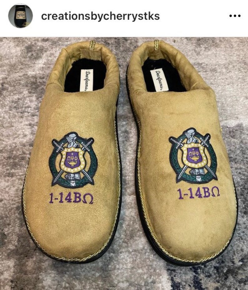 May include: A pair of tan suede slippers with black trim and a gold embroidered crest featuring a shield, swords, and the letters "N&Phi;&Phi;". The slippers also have the text "1-14&Beta;&Omega;" embroidered on the front.