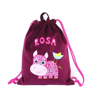 Può includere: Borsa a cordoncino bordeaux con un'applicazione di ippopotamo rosa e uccello. La borsa ha un cordoncino rosa e il nome "ROSA" è ricamato sul davanti.